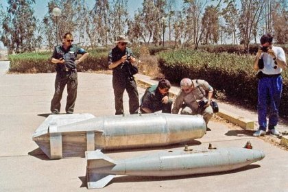 A group of 5 men examine and photograph missiles on the ground
