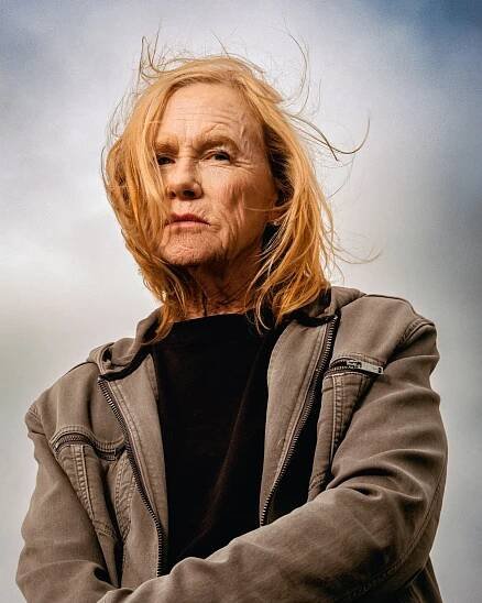 A portrait shows a windblown woman in a light brown jacket over a black top.