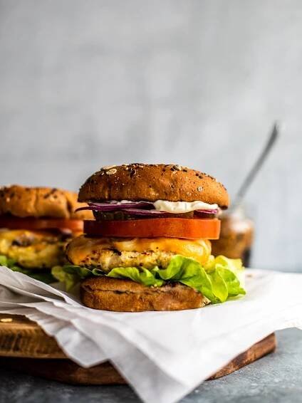 Chicken burger on a parchment-covered serving board with a chicken burger in the background.