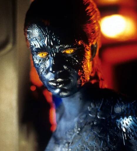 A person in intricate blue body paint and scales resembling a character from a sci-fi film, with striking yellow eyes, posing in a dramatic setting