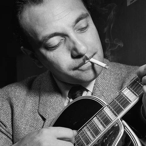 A monochrome shot of Django Reinhardt performing on his guitar while also smoking a cigarette