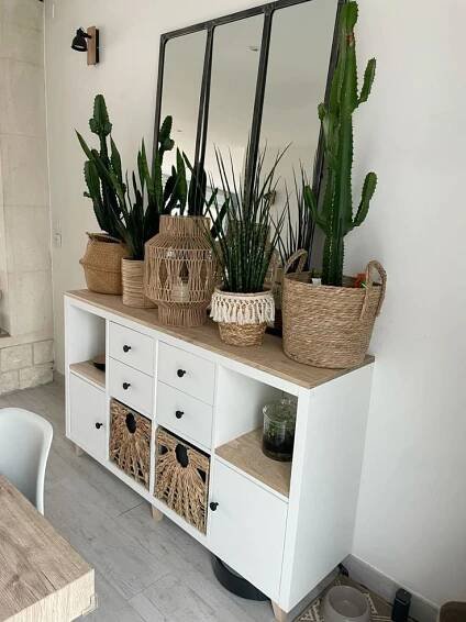 some plants are sitting on top of a white shelf with baskets and mirrors above it