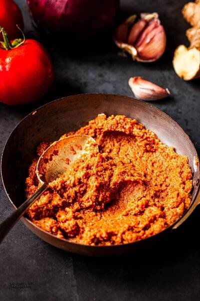 Indian base curry sauce also known as onion tomato masala in a small rustic bowl with a spoon. There is tomato, garlic and ginger too.