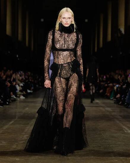 Alex Consani wearing a sheer lace black gown with a ruff while walking at the F/W 25 McQueen show.