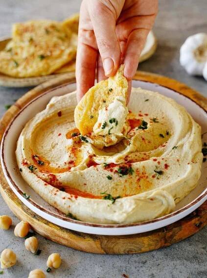 Hand taucht Fladenbrot in cremigen selbstgemachten Hummus