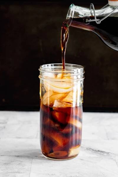 Pouring cold brew coffee into a large mason jar filled with ice. 