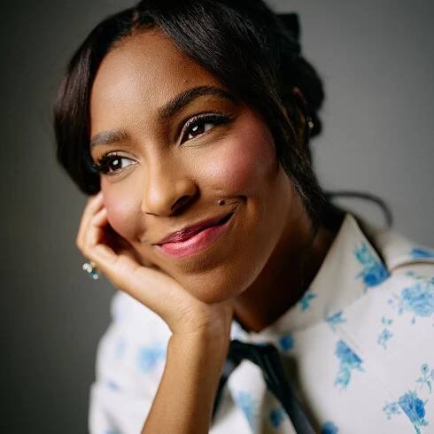 A woman smiles, leaning into her left palm that cups her face