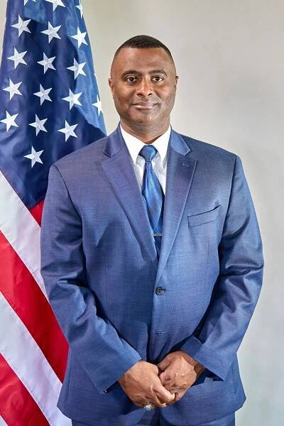 Professional photo of person in blue suit standing in front of American flag.