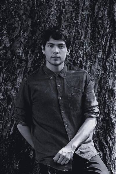 A man stands, leaning on a tree