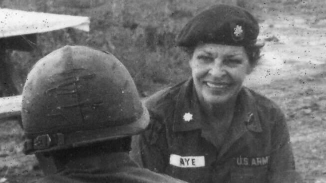 Martha Raye in conversation with members of the 173rd Airborne Brigade. Raye and the soldiers sit outside on benches.