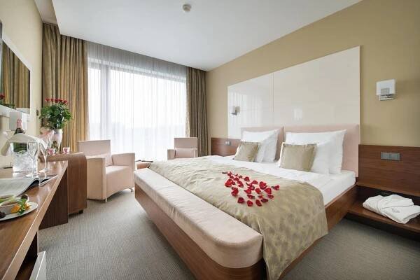 Wellness Hotel Diamant Hluboká nad Vltavou Exterior photo The photo shows a well-lit hotel room with a comfortable and inviting atmosphere. The focal point is a large bed with a light beige bedspread and several pillows, including two white pillows and two square pillows with a subtle pattern. A decorative 