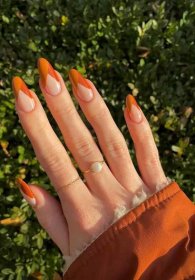 a hand with long round nails painted a nude base with burnt orange and red asymmetrical French tips