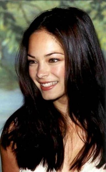 a woman with long dark hair smiling at the camera and wearing a white dress,