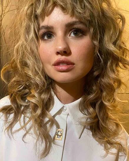 Debby Ryan wearing a long, blonde wolf cut on her curly hair