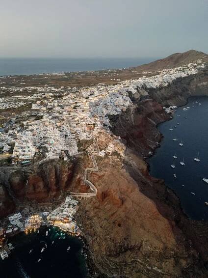 Aerial view of Santorini's iconic white buildings perched on rugged coastal cliffs overlooking the Aegean Sea.