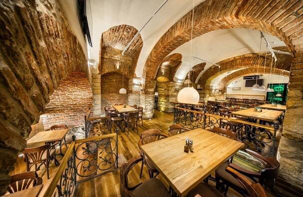 Restaurace s dřevěnými stoly a židlemi ve zděné budově.