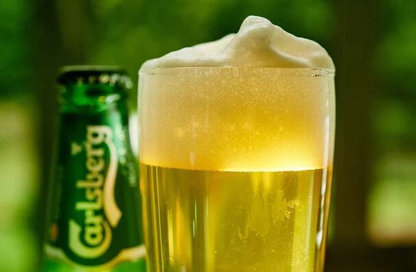 glass of carlsberg beer with a foamy head and a bottle of carlsberg slightly blurry in the background