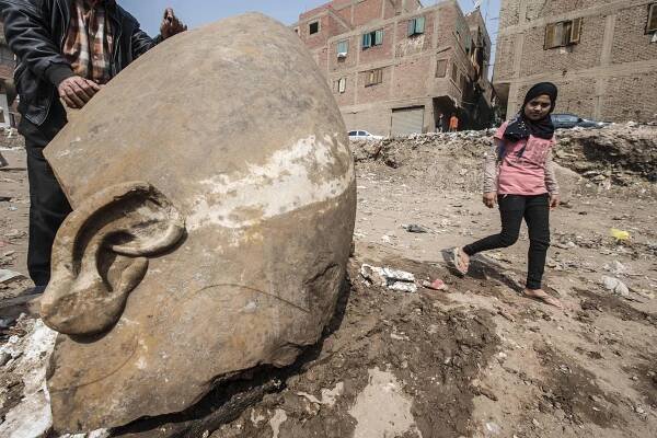 an Egyptian girl walks past the head of a statue