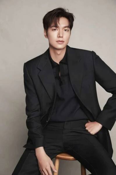 a young man sitting on top of a wooden chair wearing a black suit and tie