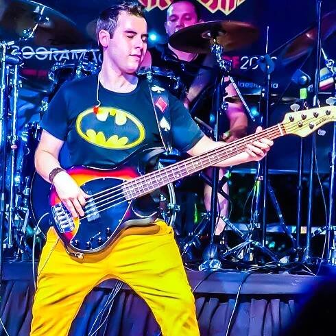 A man in yellow pants and batman shirt playing guitar.