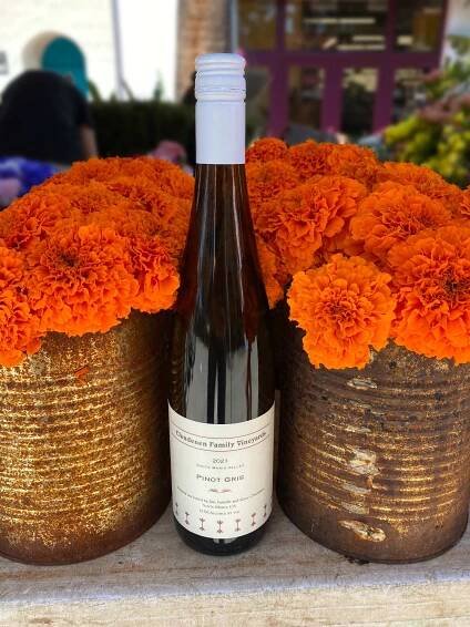 a bottle of 2021 Clendenen Family Vineyards Pinot Gris sitting between to bunches of orange marigolds in rusted vintage, tomato cans