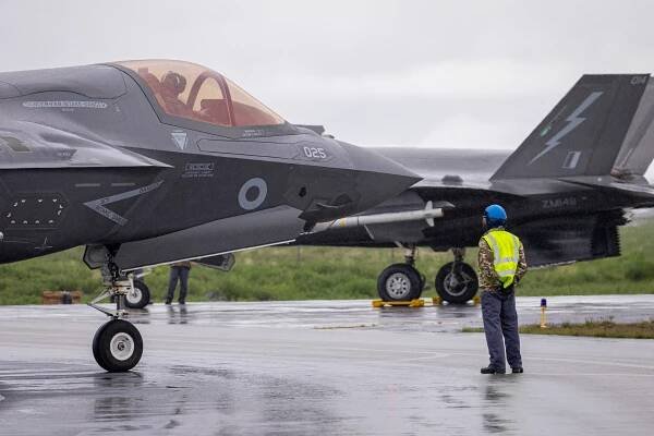 Front third of F-35 from the side, with the pilot visible in the cockpit and a serviceperson on the ground