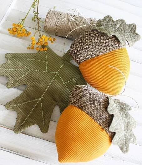 two acorns with leaves and twine on white wooden table next to yellow flowers