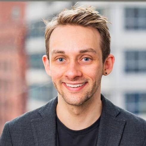 A man in a suit and black shirt is smiling for the camera.