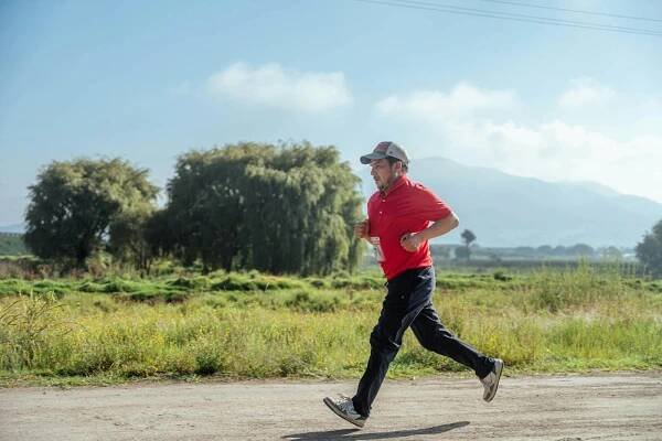 Free Adult male running on a rural dirt road, surrounded by scenic nature and hills. Stock Photo