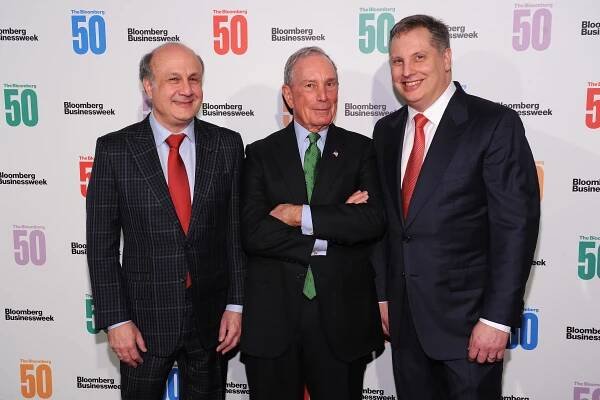 David Siegel, Michael Bloomberg and John Overdeck standing in front of a colored and white backdrop.