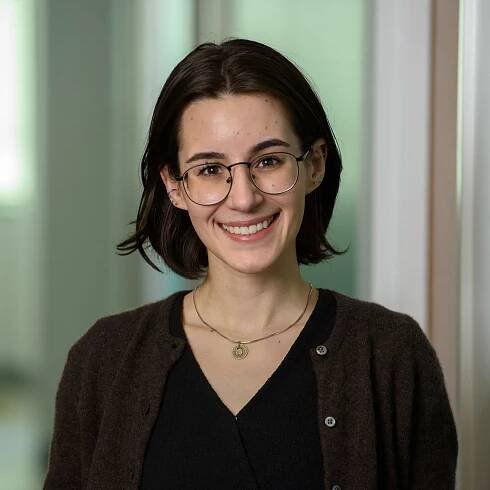 Headshot of Allison Beatty, white woman with dark brown shoulder-length hair, glasses, and a black shirt with red cardigan.