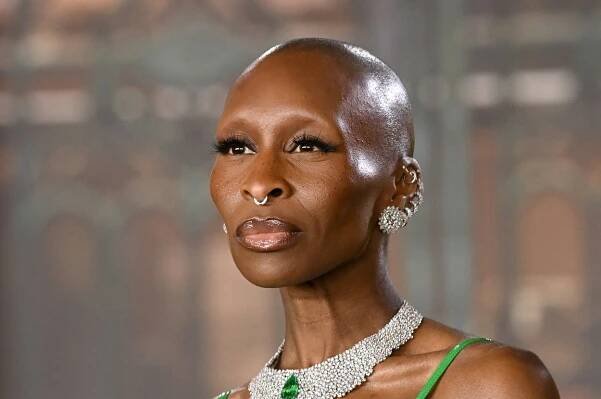 Cynthia Erivo in a green glamorous gown with a feathered boa, wearing a sparkling necklace, posing confidently at an event