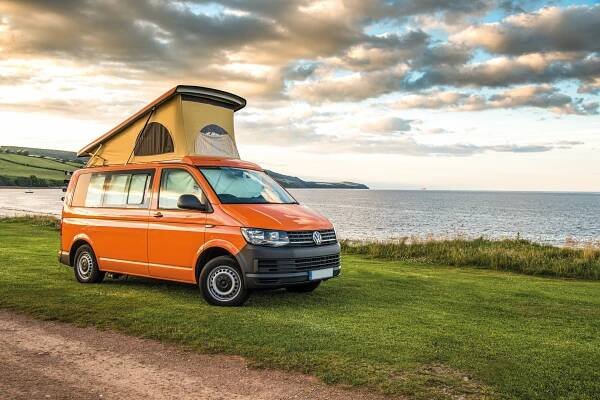 Orange camper van parked in grassy area overlooking the sea.