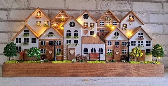 a wooden house with plants and lights on the windowsill is displayed in front of a brick wall