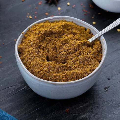 Curry Powder in a white bowl with few ingredients scattered around.