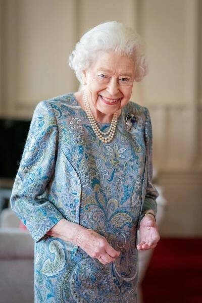 Queen Elizabeth II smiling in a patterned dress.