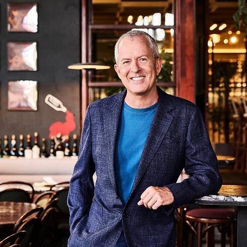 Mark Gibson leaning on a table in a restaurant with lots of dark wood and shining glass.
