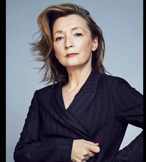 Headshot of Lesley Manville in a smart navy blue and maroon striped suit jacket looking directly at the camera with a serious and interesting expression.