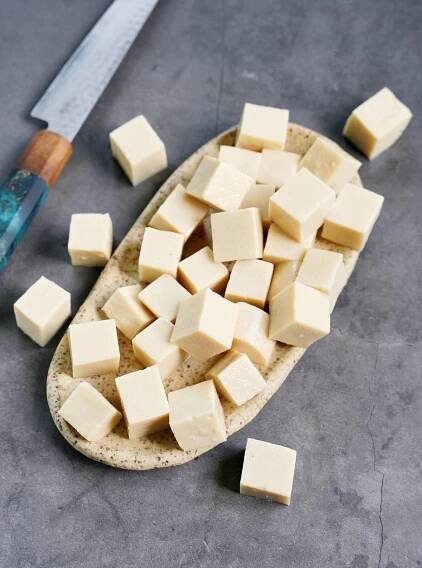 cubed homemade silken tofu on ceramic plate with knife on the side