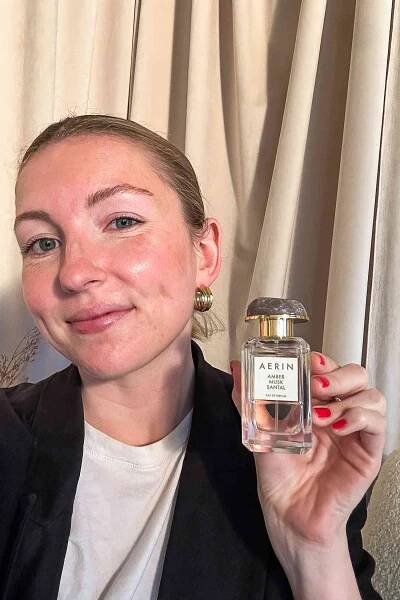 A person holding a bottle of the Aerin Amber Musk Santal perfume