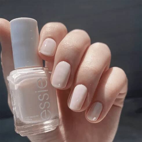 Manicured hand holding a bottle of nail polish labeled Essie