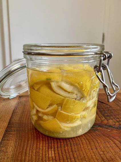 Sugary lemon rinds in an open glass flip-top jar are just barely covered with water to make lemon rind soda