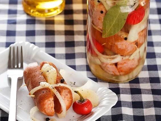 two hot dogs are on a plate next to a jar of pickles and tomatoes