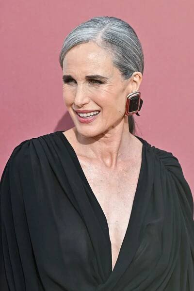 Andie MacDowell with gray hair against a pink background