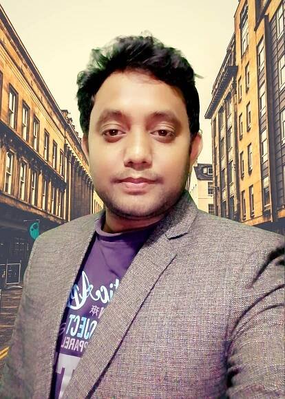 A man in a suit and a purple shirt is taking a selfie in front of a city street.
