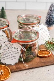 Three jars with oranges and pine cones on a wooden cutting board, perfect for creating homemade potpourri or holiday simmer pot.
