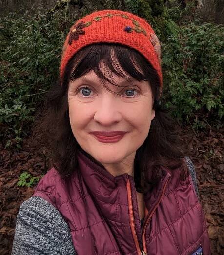 Heeadshot of a woman with blue eyes and dark hair in a beanie hat.