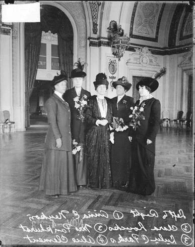 [British suffragist Mrs. Emmeline Pankhurst (center) standing with policewomen Anna E. Neukon, Clara Loucks, LuLu C. Parks and Mrs. Alice Clement (left to right) inside the Hotel LaSalle].