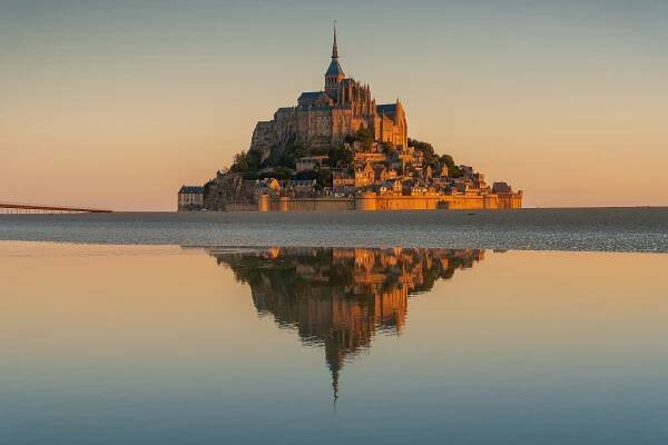 Přílivový ostrov Mont-Saint-Michel během východu slunce, zrcadlící se na hladině při nejvyšším odlivu