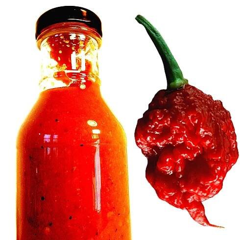A bottle of Carolina Reaper hot sauce, along with a fresh Carolina pepper on the side.